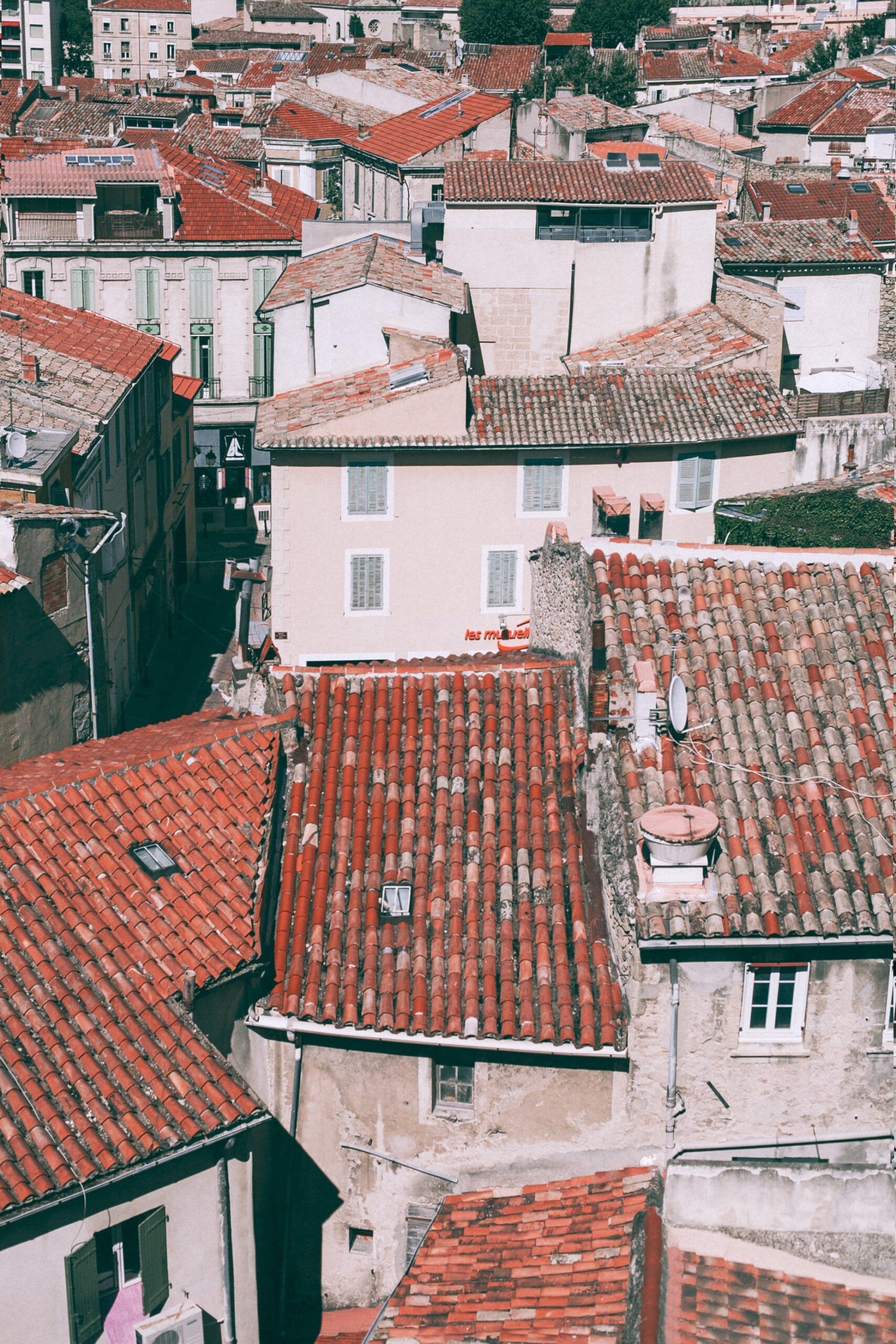 Vista elevada de edificios con tejados de tejas rojizas, fachadas claras, ventanas, chimeneas, canalones y antenas parabólicas.